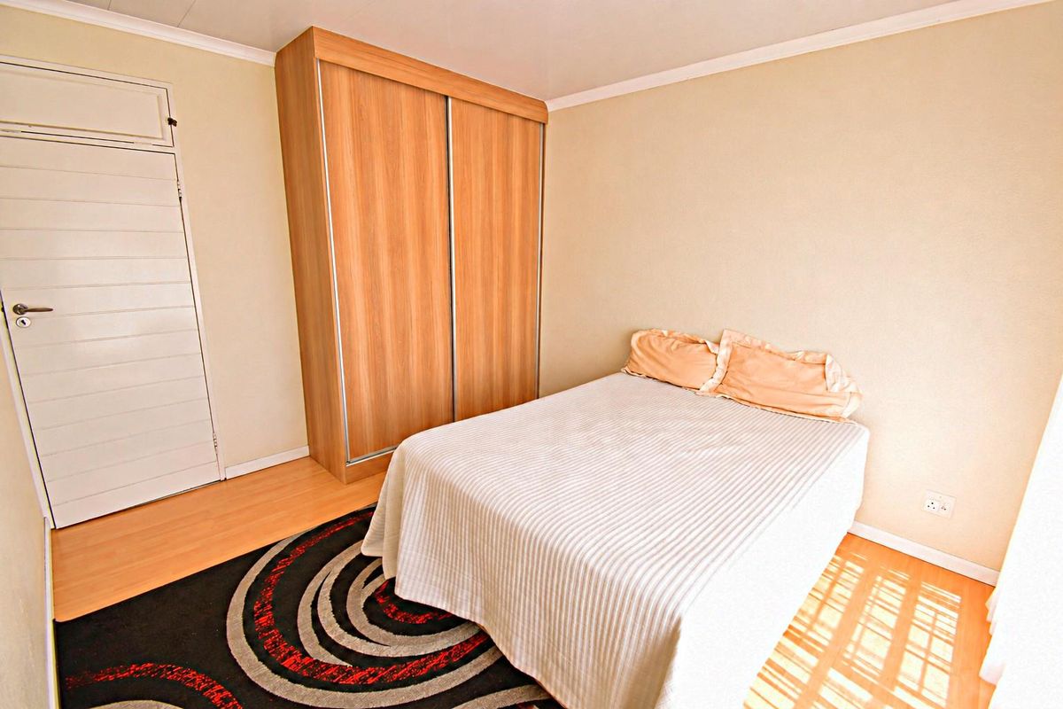A functional bedroom featuring laminate flooring and a built-in wooden wardrobe, providing practical storage space.