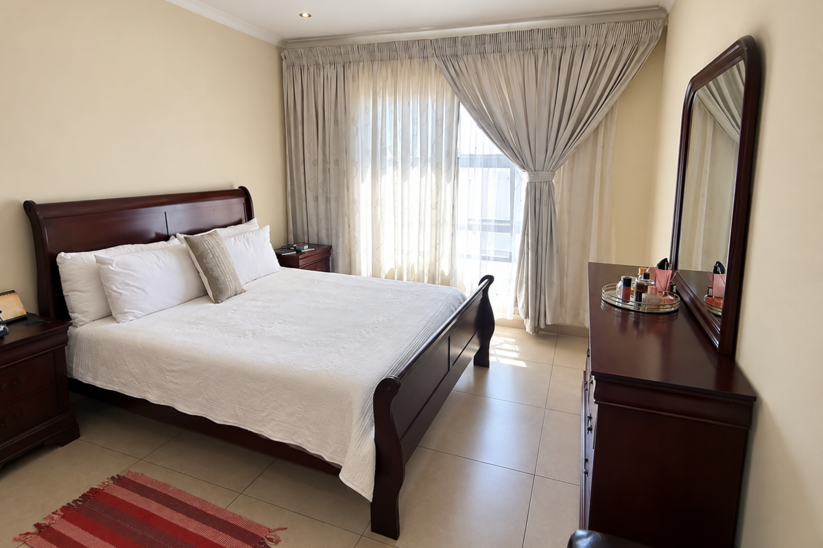 A well-maintained bedroom featuring neutral wall tones, tiled flooring, and large window with integrated curtain tracks, providing a bright and comfortable living space.