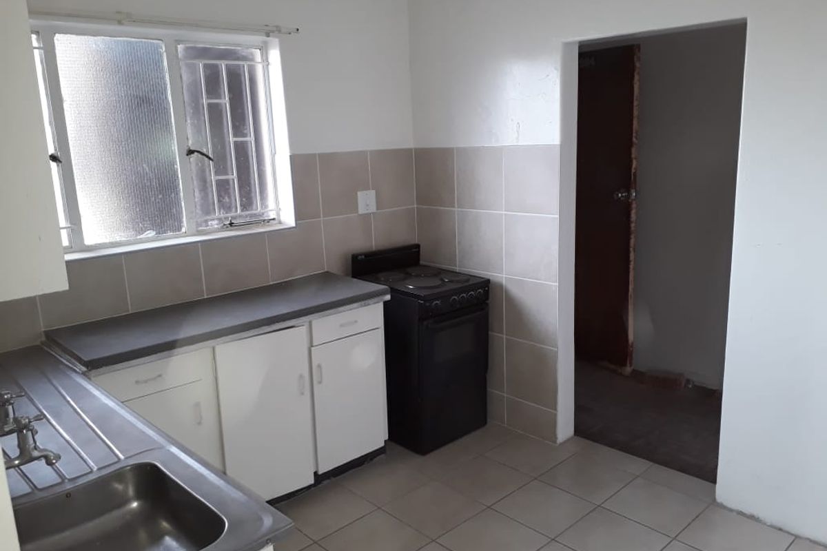 A functional kitchen featuring tiled flooring, a stainless steel sink, built-in cabinetry, and a freestanding stove, ready for modernization.