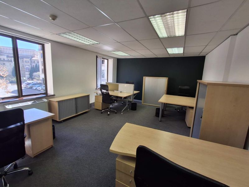 A functional office space featuring carpeted flooring, suspended ceilings with recessed lighting, and large windows providing natural light.