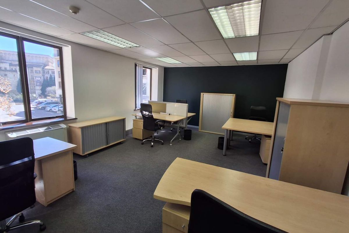 A functional office space featuring carpeted flooring, suspended ceilings with recessed lighting, and large windows providing natural light.