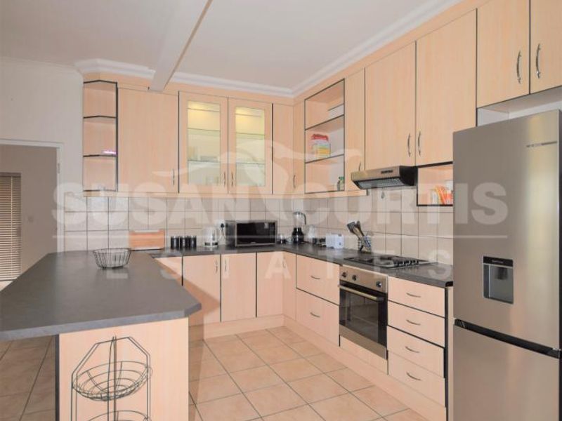 A functional kitchen featuring light wood-finish cabinetry, dark laminate countertops, tiled flooring, and integrated appliances including an oven and hob.