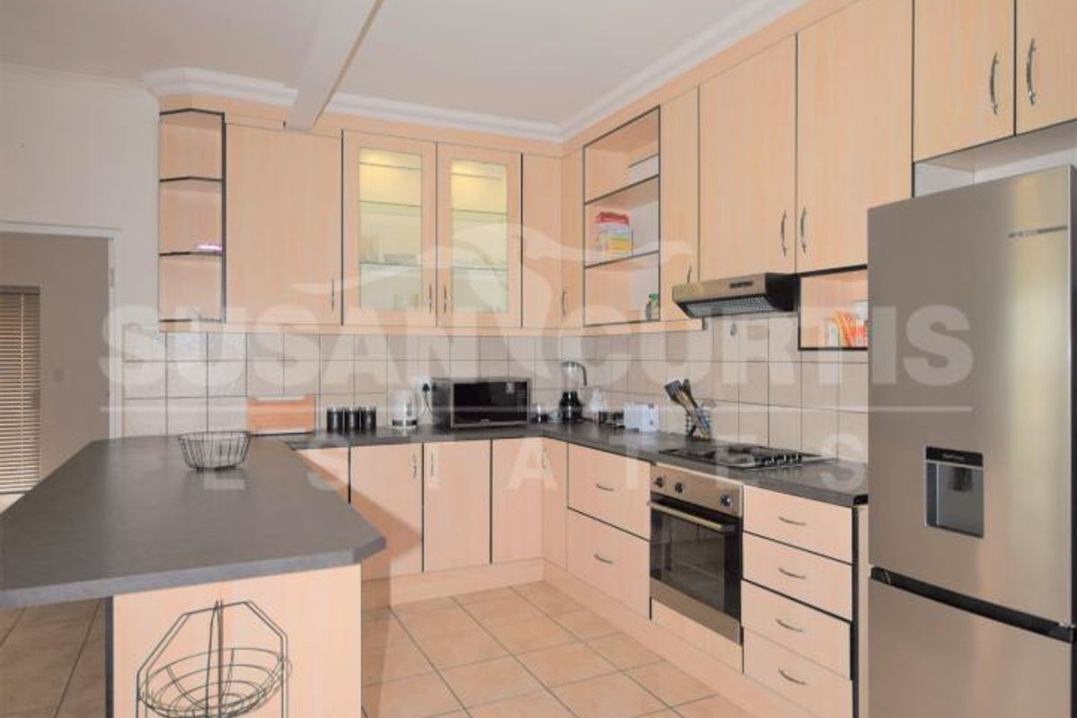 A functional kitchen featuring light wood-finish cabinetry, dark laminate countertops, tiled flooring, and integrated appliances including an oven and hob.