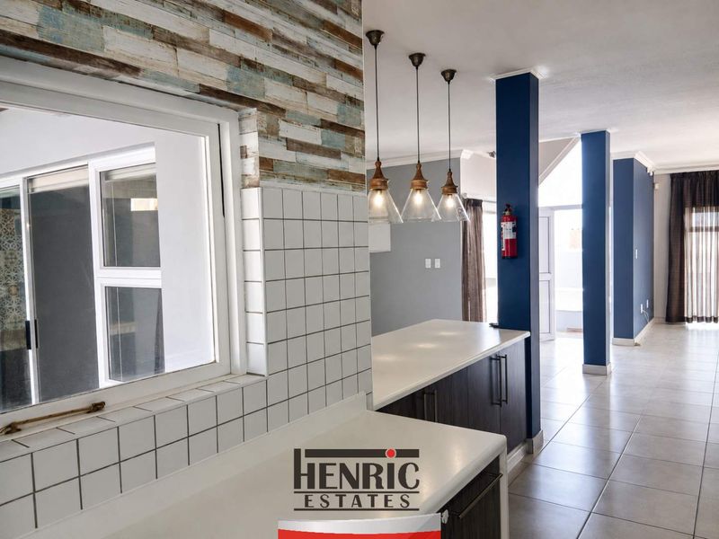 Open plan living area featuring a kitchen island with pendant lighting, tiled flooring, and structural columns, offering a versatile space for modern living.