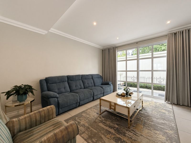 A bright and well-maintained living room featuring tiled flooring, recessed downlighting, crown molding, and a large glass sliding door providing natural light.