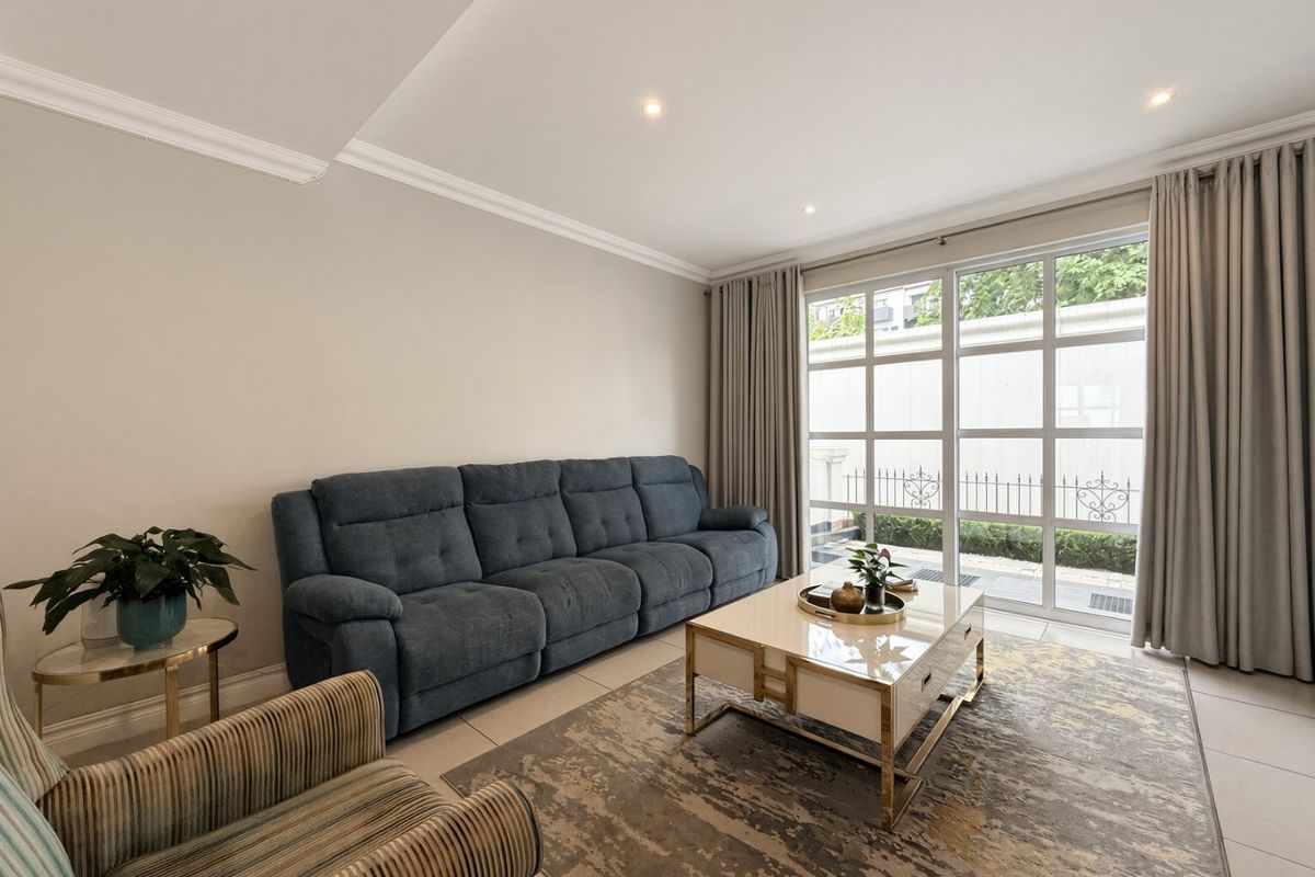 A bright and well-maintained living room featuring tiled flooring, recessed downlighting, crown molding, and a large glass sliding door providing natural light.