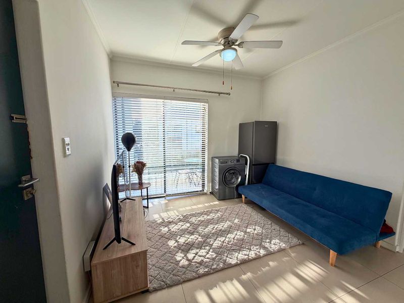 A compact living area featuring tiled flooring, a ceiling fan, and a sliding glass door with venetian blinds providing natural light.