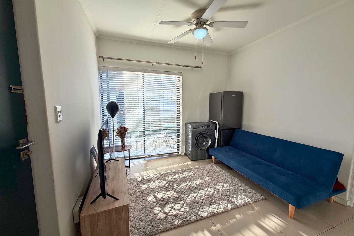 A compact living area featuring tiled flooring, a ceiling fan, and a sliding glass door with venetian blinds providing natural light.