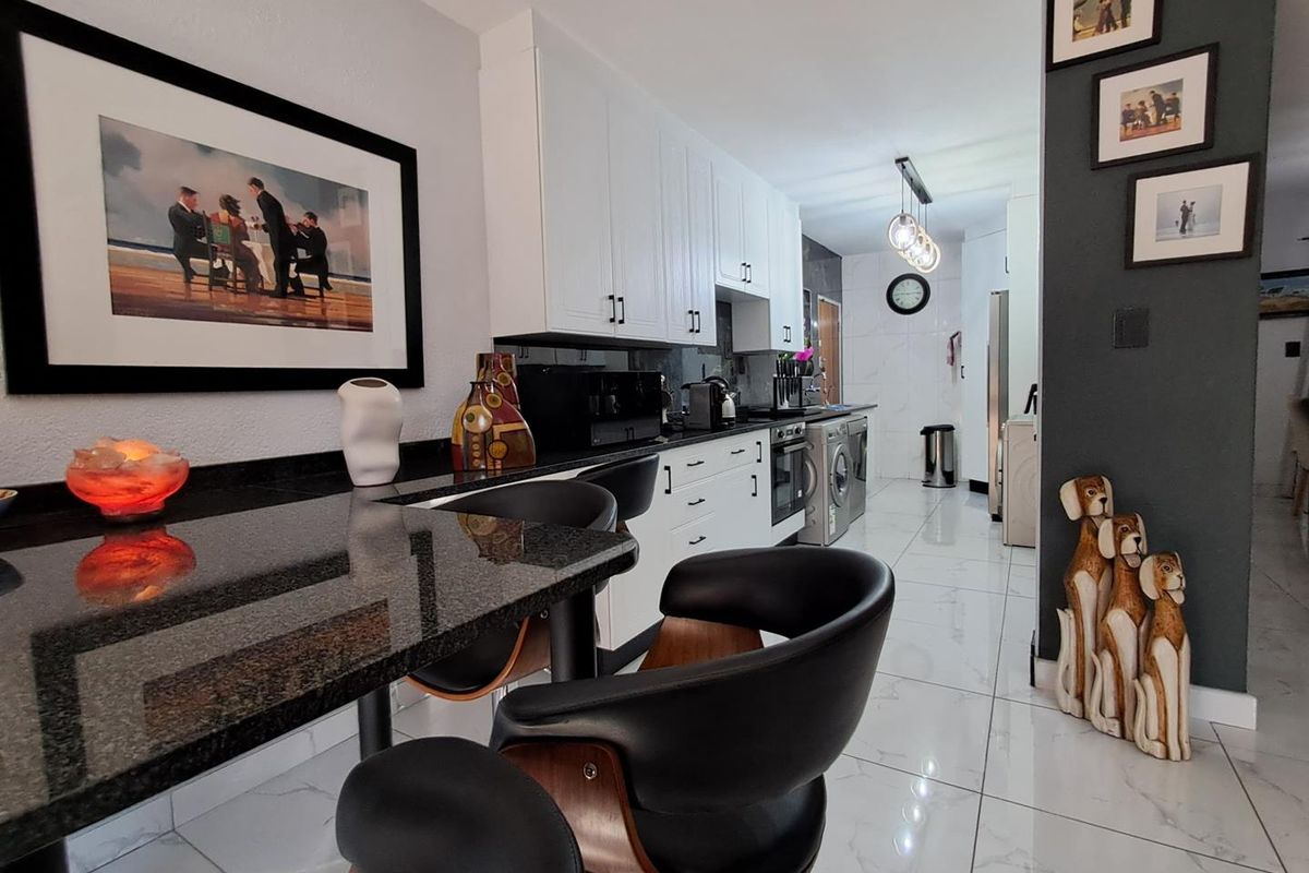Modern kitchen featuring white cabinetry, dark granite countertops, a breakfast bar, and polished marble-look floor tiles.