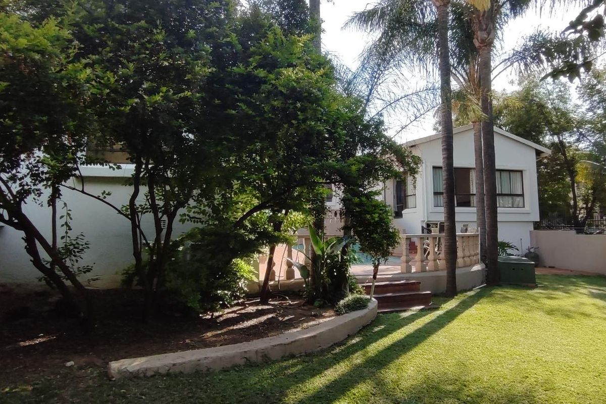 Rear garden view featuring a swimming pool, stone balustrade, and established landscaping with a lawn area.