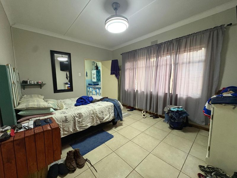 A bedroom featuring tiled flooring, a ceiling fan, and large windows with curtain rails, providing access to an adjacent room.