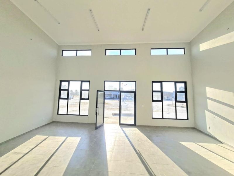 A bright, spacious, and modern open-plan office area featuring high ceilings, large windows, and tiled flooring, offering a clean and professional workspace.
