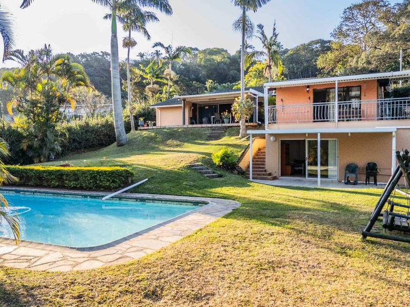 Rear view of a multi-level house featuring a swimming pool, covered patio, balcony, and landscaped garden area.