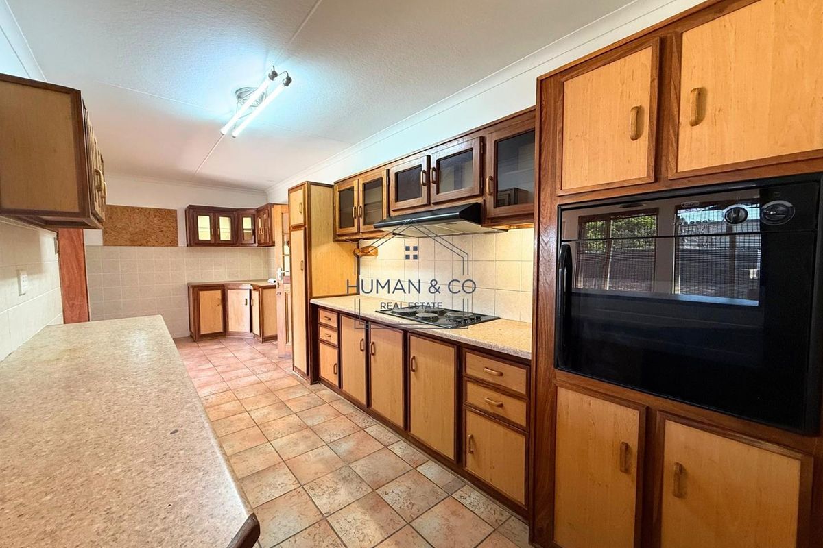 A functional kitchen featuring timber-framed cabinetry, built-in oven, integrated hob, extractor fan, and tiled flooring with ample counter space.