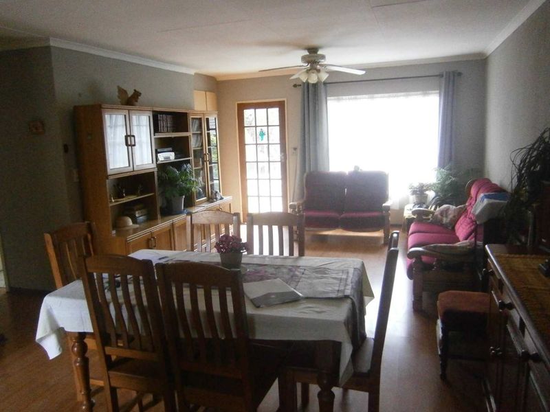 Open-plan living and dining area featuring laminate flooring, a ceiling fan, and a timber-framed glass door leading to the exterior.