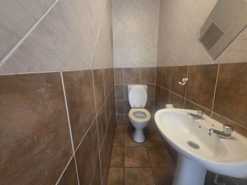 A compact guest bathroom featuring a pedestal basin and toilet with neutral-toned ceramic wall and floor tiling.