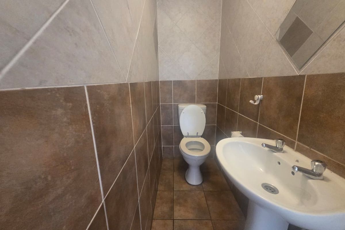 A compact guest bathroom featuring a pedestal basin and toilet with neutral-toned ceramic wall and floor tiling.