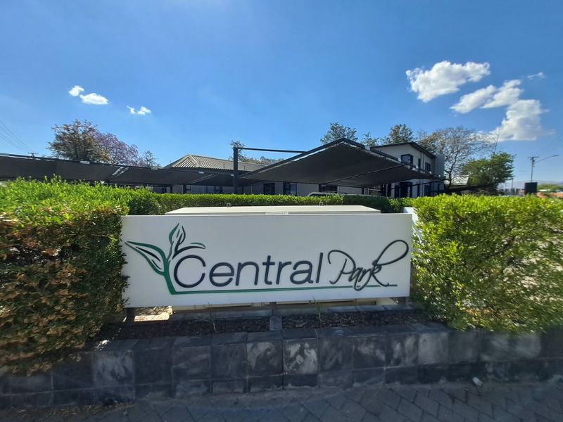 Front entrance view of Central Park office complex featuring professional signage, manicured hedging, and shaded parking structures.