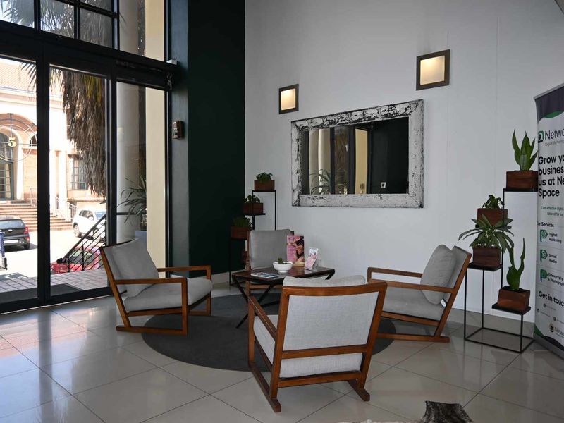 A bright and modern office entrance area featuring high ceilings, large glass sliding doors, and polished tiled flooring.