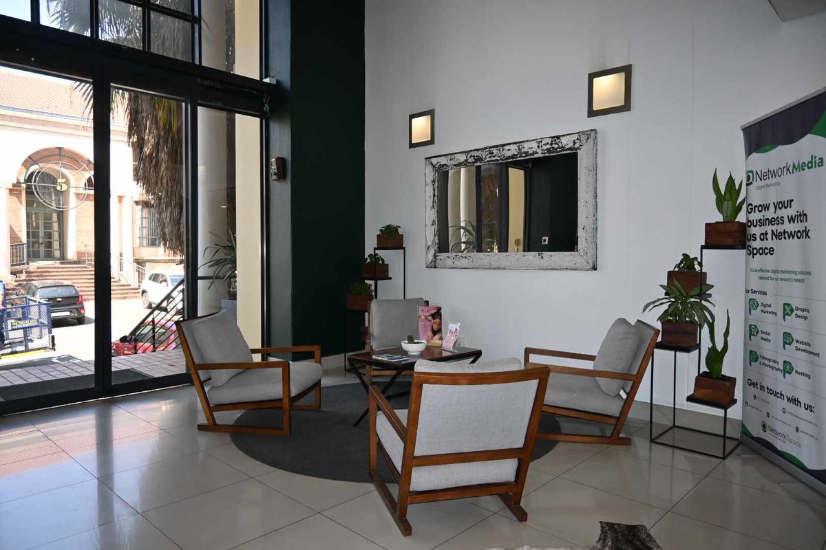A bright and modern office entrance area featuring high ceilings, large glass sliding doors, and polished tiled flooring.