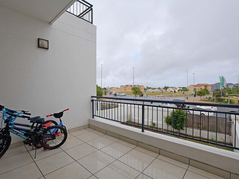 A tiled balcony featuring a metal balustrade and an exterior wall light, offering an open view of the surrounding neighborhood.
