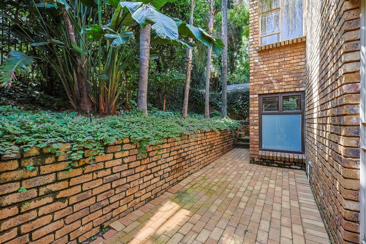 A private side courtyard featuring brick paving, a low retaining wall, and established garden greenery adjacent to the house exterior.