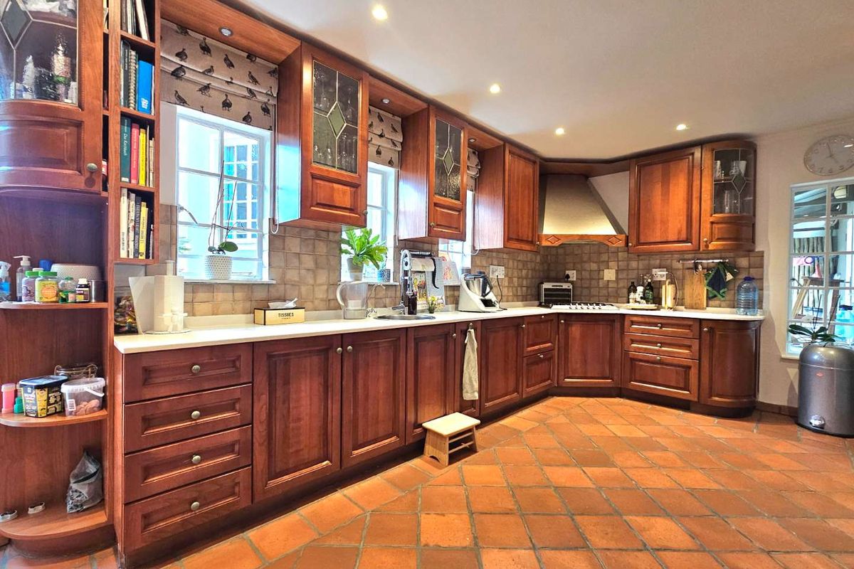 A traditional kitchen featuring warm-toned wooden cabinetry, tiled countertops, a built-in extractor fan, and terracotta floor tiles.