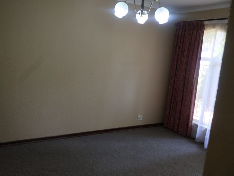 An empty bedroom featuring carpeted flooring, a central ceiling light fixture, and a window with installed curtain rods.