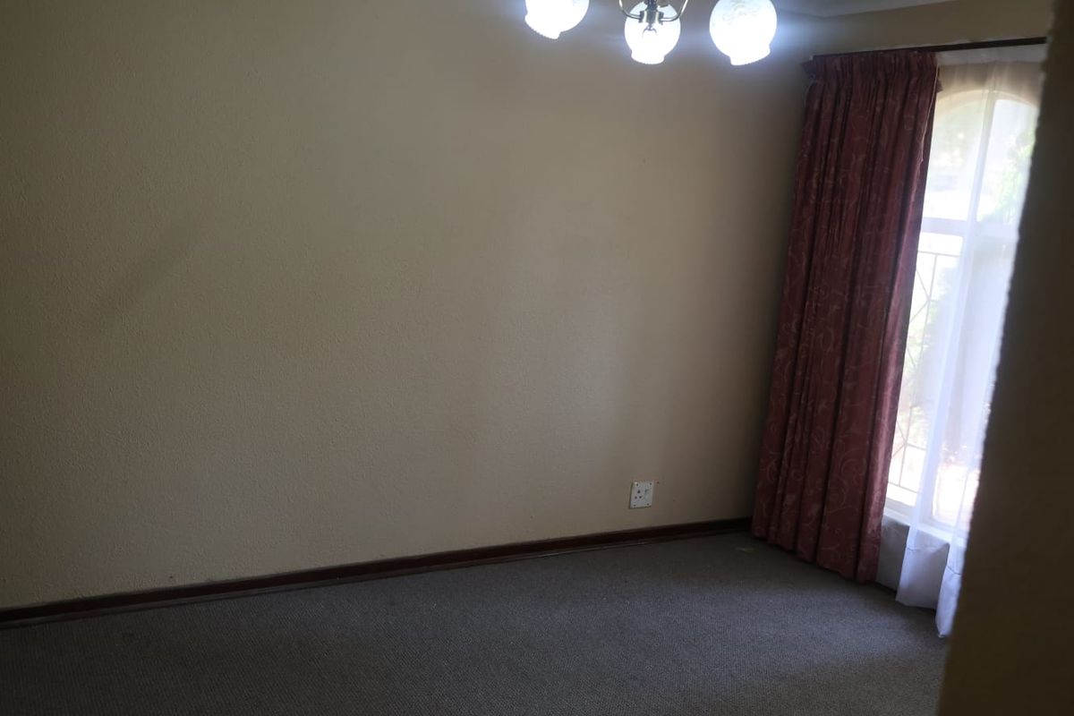 An empty bedroom featuring carpeted flooring, a central ceiling light fixture, and a window with installed curtain rods.