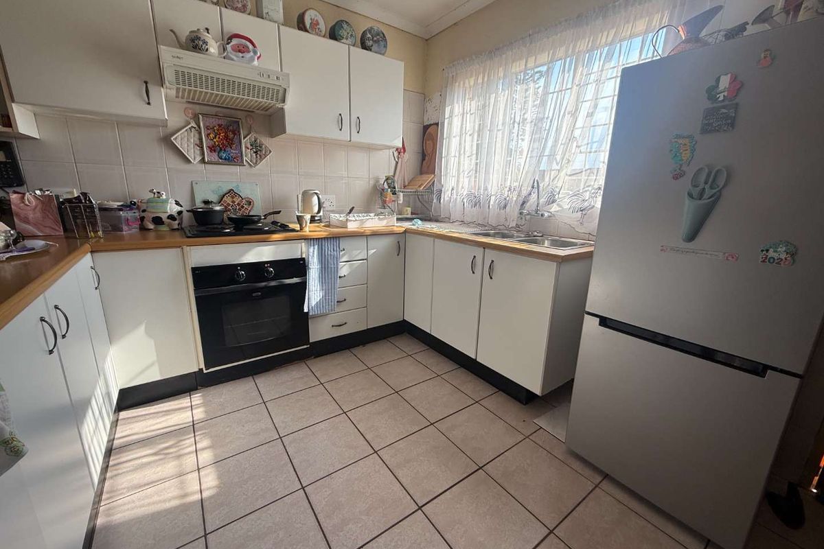 A functional kitchen featuring white cabinetry, a built-in oven, extractor fan, and tiled flooring with a double sink under a window.