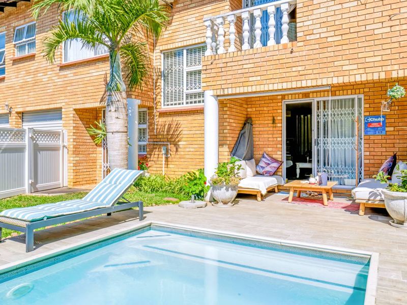 A private outdoor pool area featuring a tiled patio, brick townhouse facade, and a balcony with decorative balustrades.