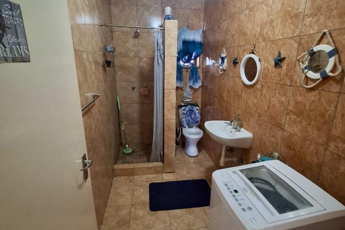 A functional bathroom featuring floor-to-ceiling tiled walls, a walk-in shower enclosure, a pedestal basin, and a toilet.