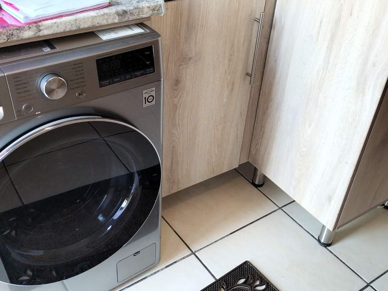 A functional laundry area featuring modern wood-finish cabinetry, stone countertops, and tiled flooring.