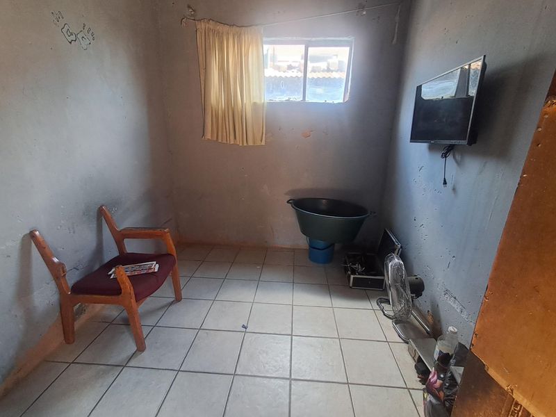 A small bedroom featuring tiled flooring and a sliding window, currently requiring significant cosmetic updates and wall finishing to improve its overall condition.
