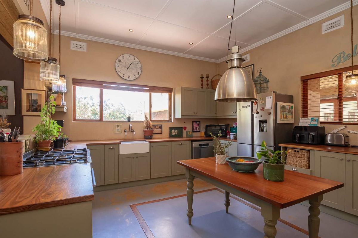 A charming kitchen featuring sage green cabinetry, wooden countertops, a farmhouse sink, and a central wooden island, creating a warm and functional culinary space.