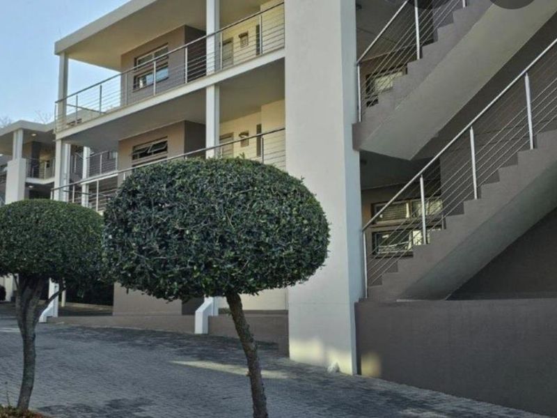 Modern apartment complex exterior featuring multi-level balconies with stainless steel balustrades, external staircases, and a paved driveway area.