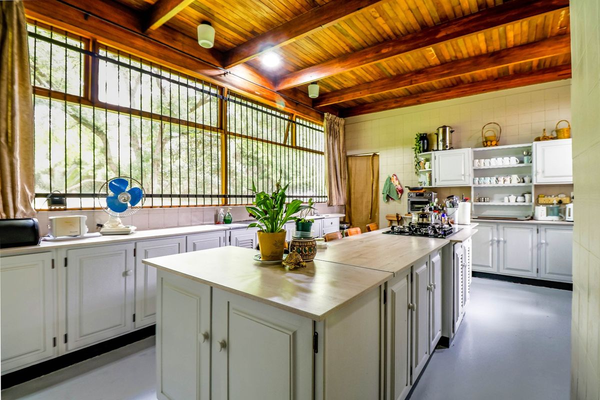 Spacious farmhouse kitchen featuring a central island, built-in cabinetry, gas hob, and a distinctive exposed timber beam ceiling with large windows.