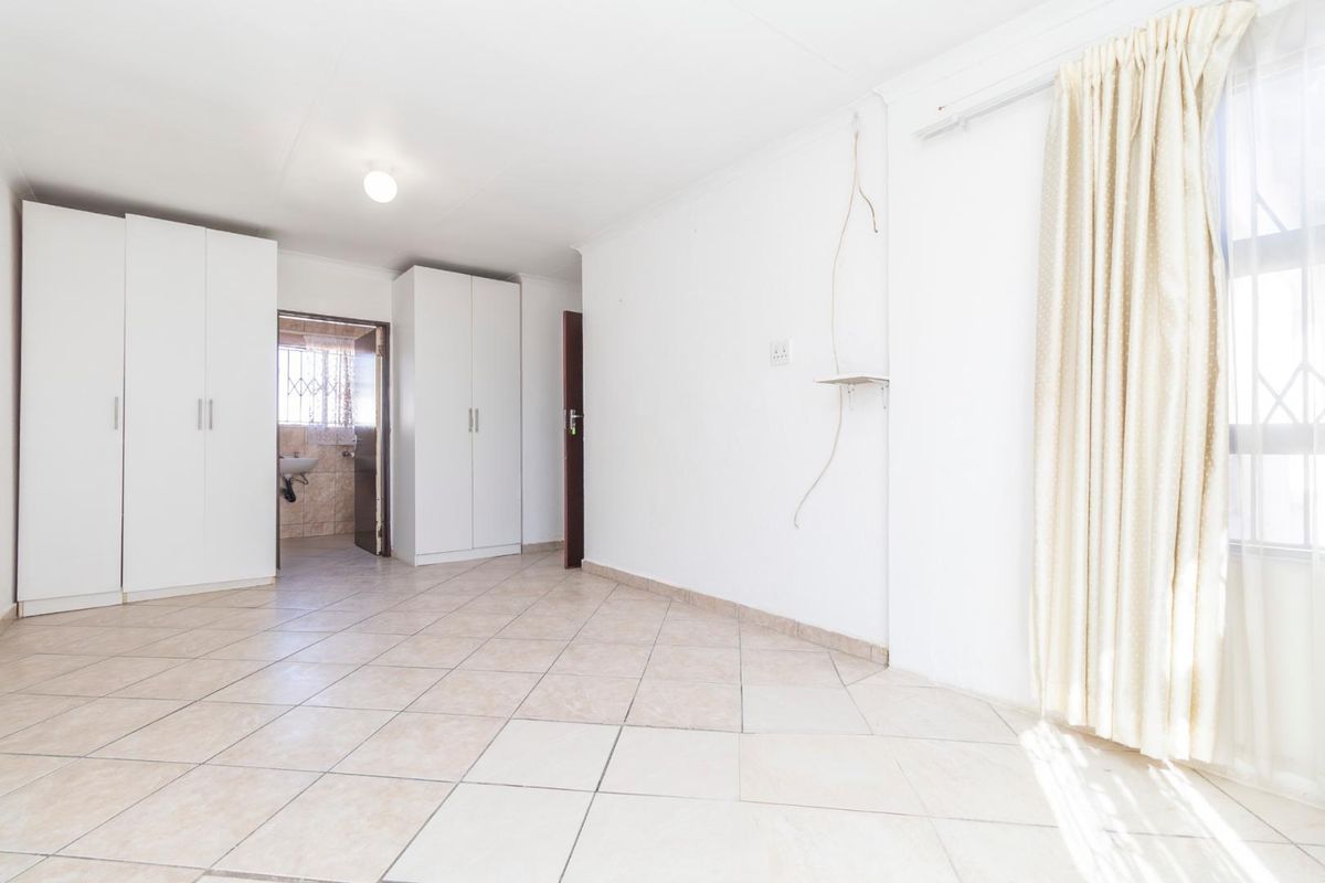 A bright bedroom featuring tiled flooring, built-in wardrobes, and an en-suite bathroom entrance, offering a clean and functional living space.