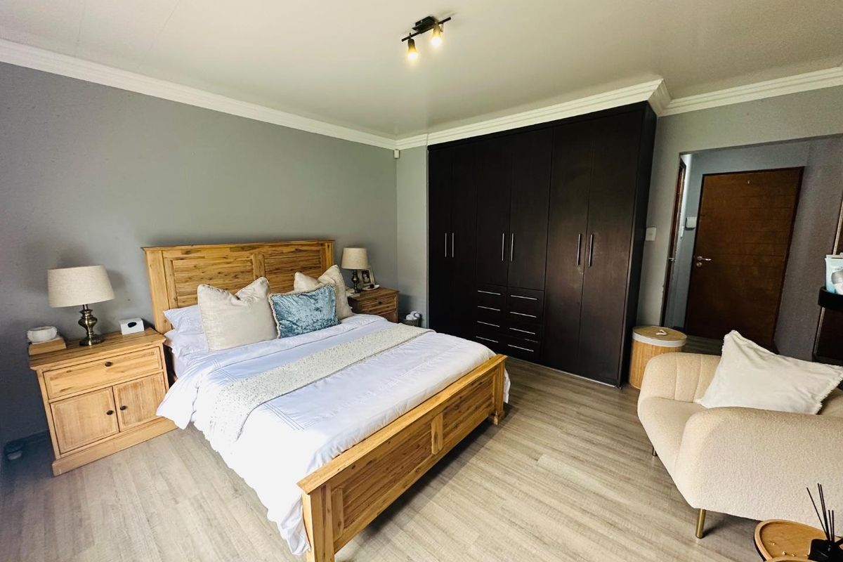 A well-maintained bedroom featuring laminate flooring, neutral wall tones, and extensive dark wood built-in cupboards for ample storage.