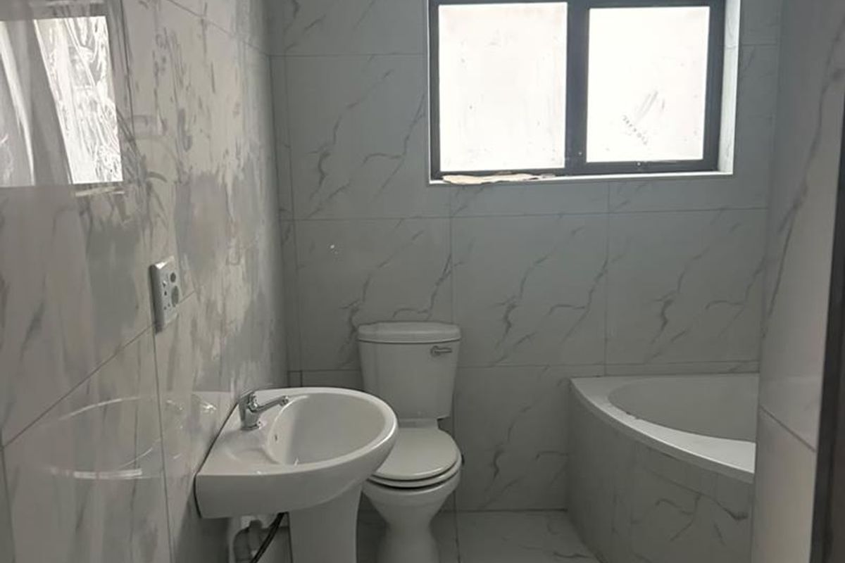 A modern, empty bathroom featuring marble-look wall and floor tiles, a pedestal basin, a toilet, and a built-in bathtub.