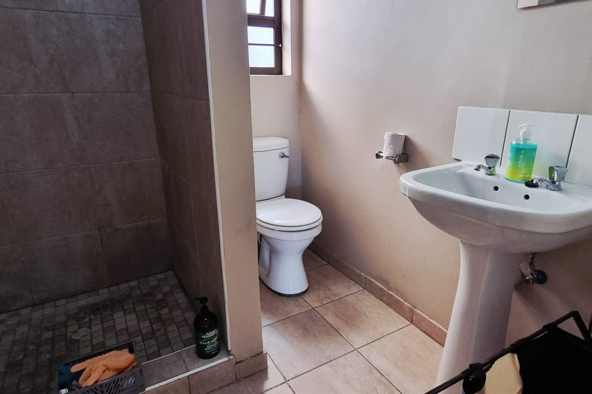 A functional bathroom featuring a walk-in shower with tiled walls, a pedestal basin, and a standard toilet.