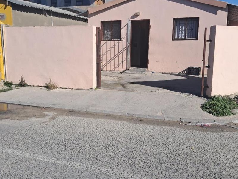 Front exterior view of a single-story house featuring a perimeter wall, security gate, and concrete driveway access.