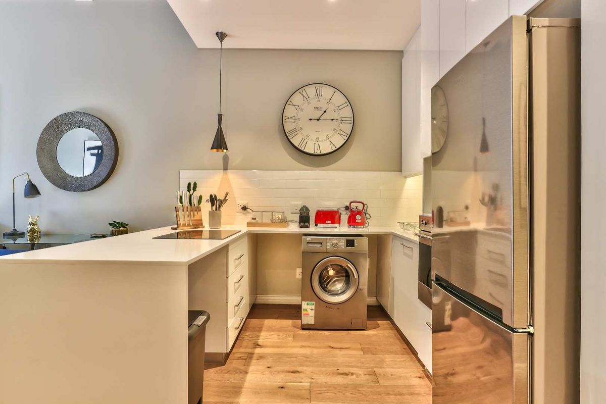 Modern kitchen featuring sleek white cabinetry, stone countertops, subway tile backsplash, integrated appliances, and warm hardwood flooring.