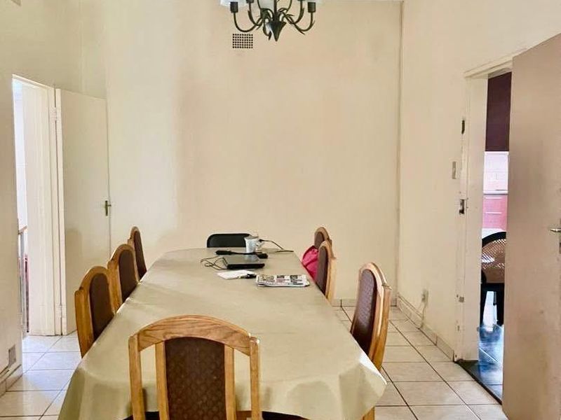 A dining room featuring ceramic floor tiles, a central chandelier, and decorative ceiling cornicing, offering a functional space for family meals.