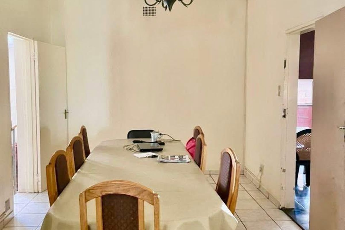 A dining room featuring ceramic floor tiles, a central chandelier, and decorative ceiling cornicing, offering a functional space for family meals.