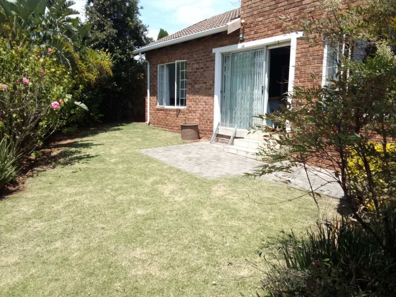 Rear view of the townhouse featuring a brick facade, a paved patio area, and a well-maintained lawn with established garden borders.
