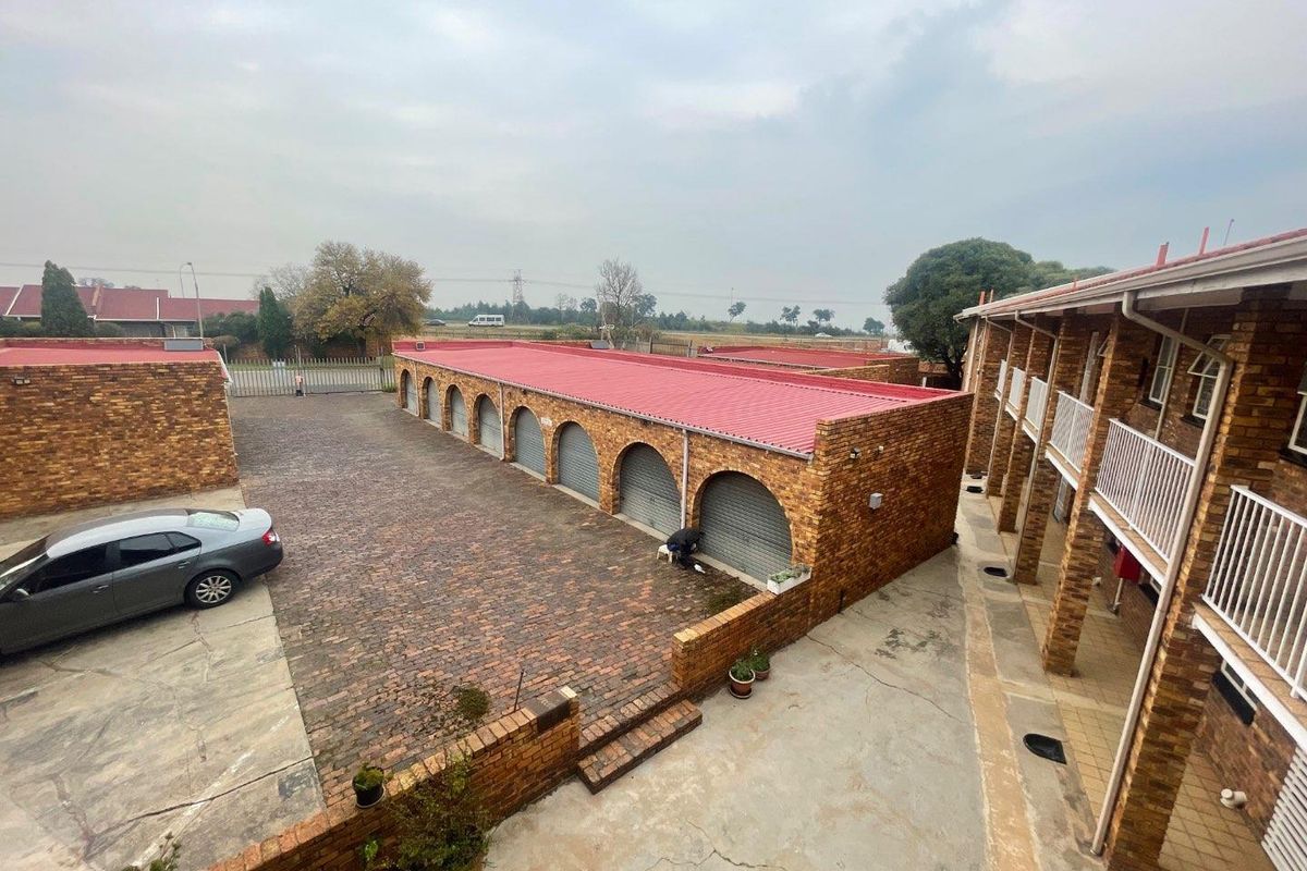 An elevated view of the apartment complex courtyard featuring a row of garages with arched brick detailing and paved communal areas.