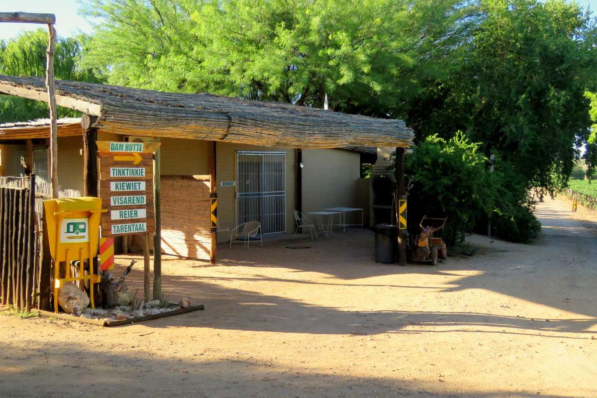A rustic farm-style outdoor area featuring a thatched roof patio, directional signage, and a dirt driveway leading towards the property grounds.