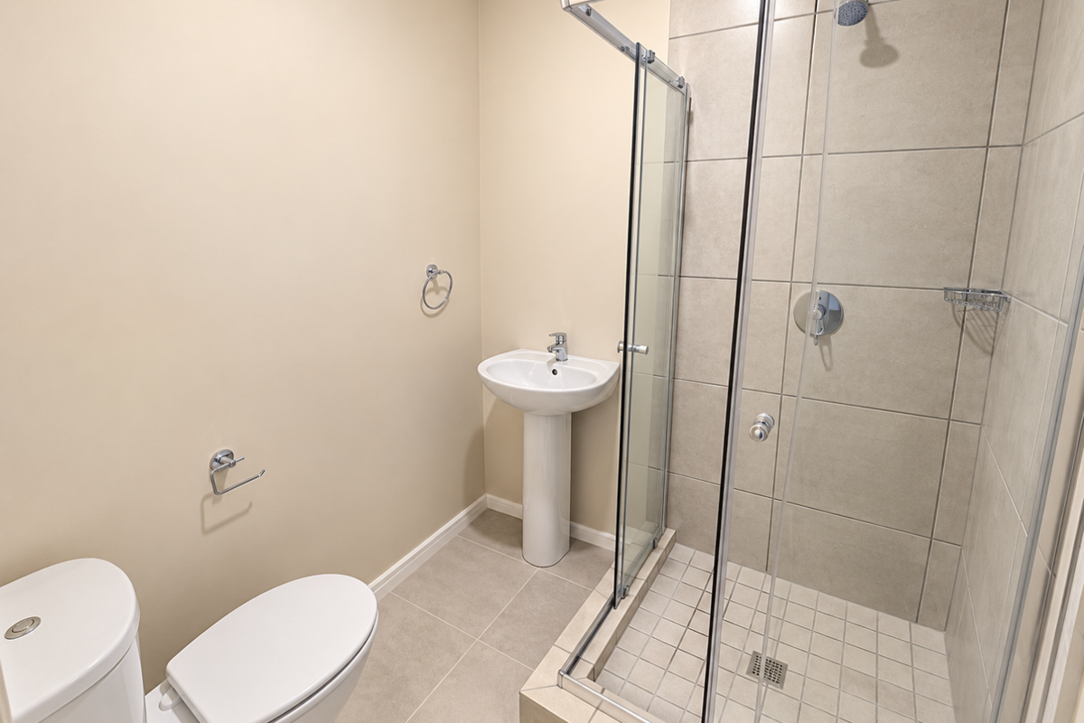 A clean, modern bathroom featuring a pedestal basin, a glass-enclosed shower with tiled walls, and a standard toilet.
