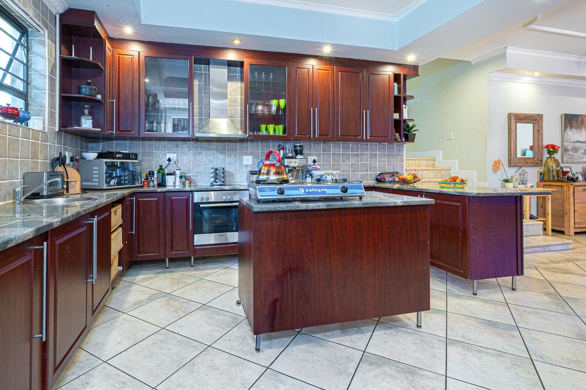 A functional kitchen featuring dark wood cabinetry, granite countertops, a central island, built-in oven, and stainless steel extractor fan.